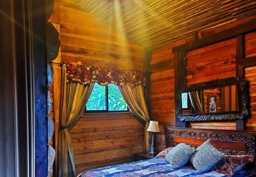 Habitación de la cabaña de día, con cama, madera y luz del jardín