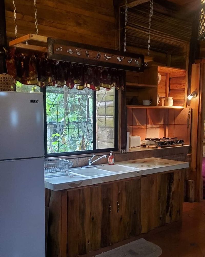 Cocina rústica de la cabaña con refrigeradora y ventana al jardín