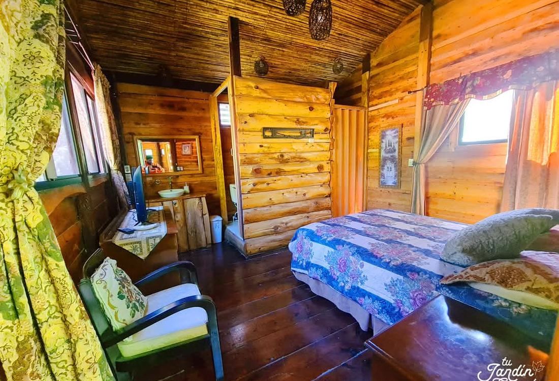 Interior de la cabaña: cama, sillón y baño en madera