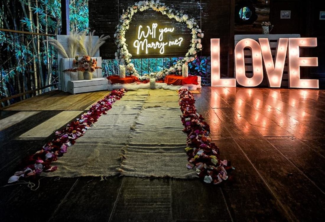 Terraza de madera con letras LOVE, pétalos y arco floral para propuesta de matrimonio